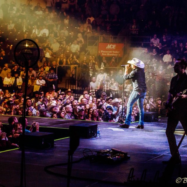 Justin Moore singing in spotlight, crowded arena view