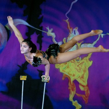 Female circus performer balancing on one hand on stilts.